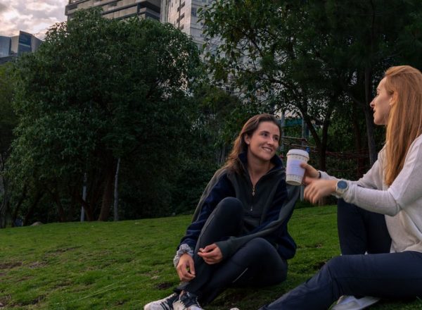 Two women enjoying coffee and conversation in a vibrant park setting in Mexico City.